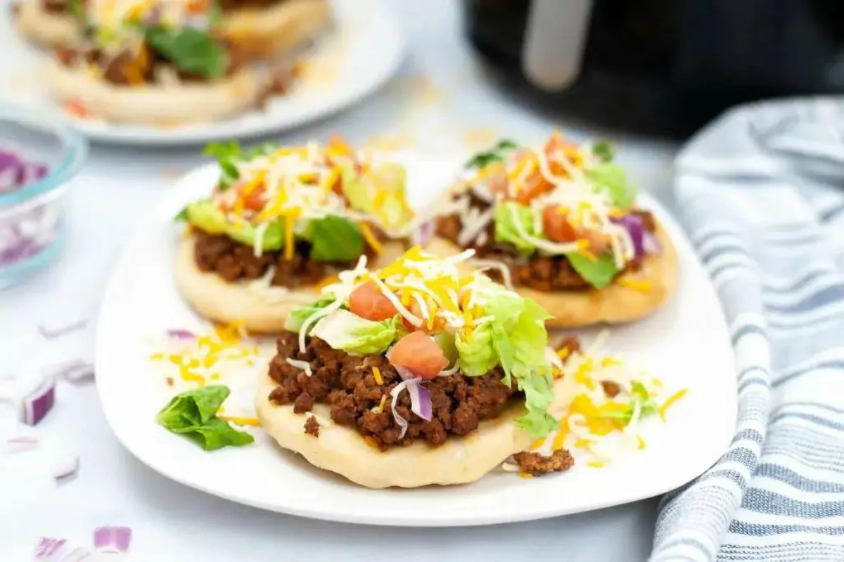 Three fry bread tacos on a plate with lettuce, tomato and cheese over the top.