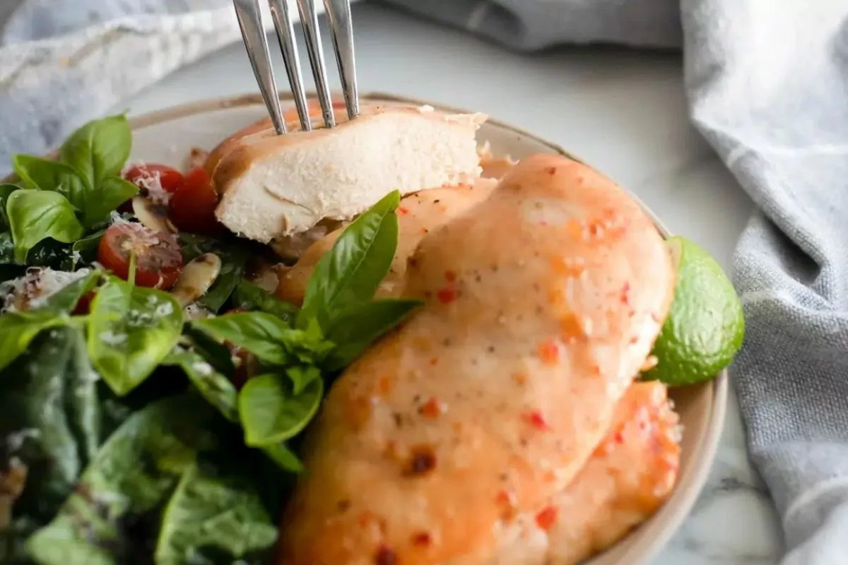 piece of chicken on fork held over plate of chicken cutlets and salad.