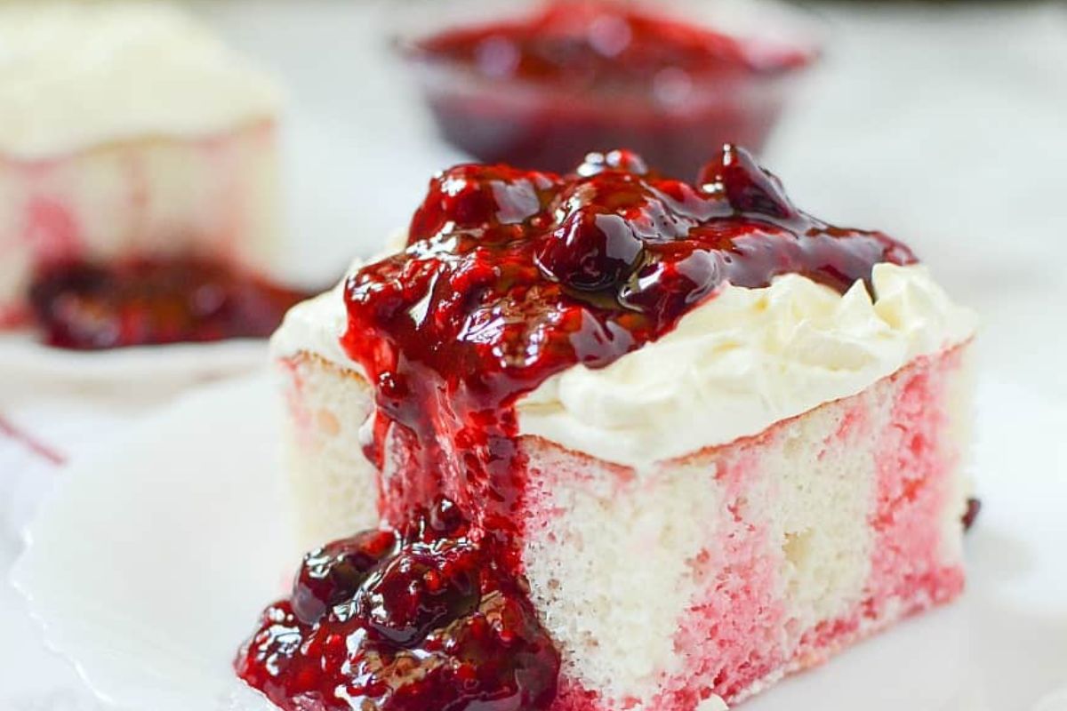 a slice of white cake with jello inside and berry compote over the fluffy frosting.