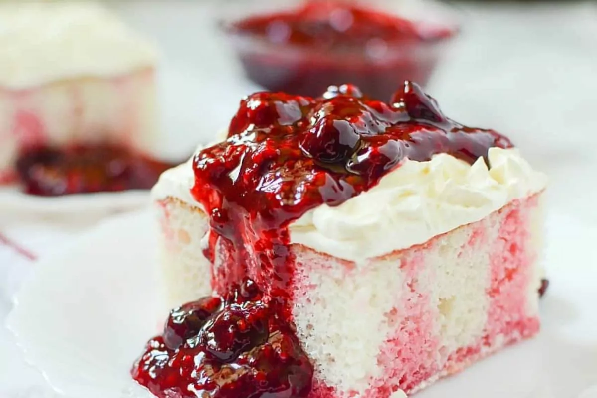 a slice of white cake with jello inside and berry compote over the fluffy frosting.