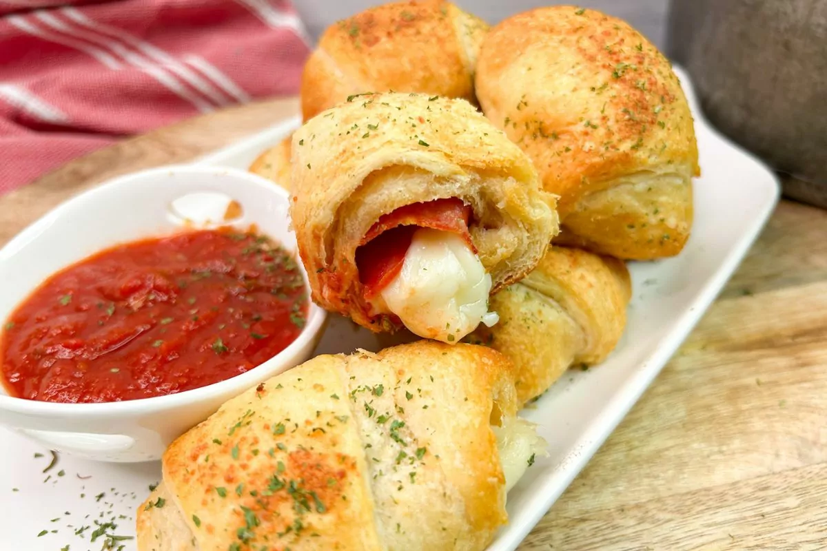 crescent rolls with pepperoni, mozzarella cheese on white plate with small bowl of tomato sauce for dipping.