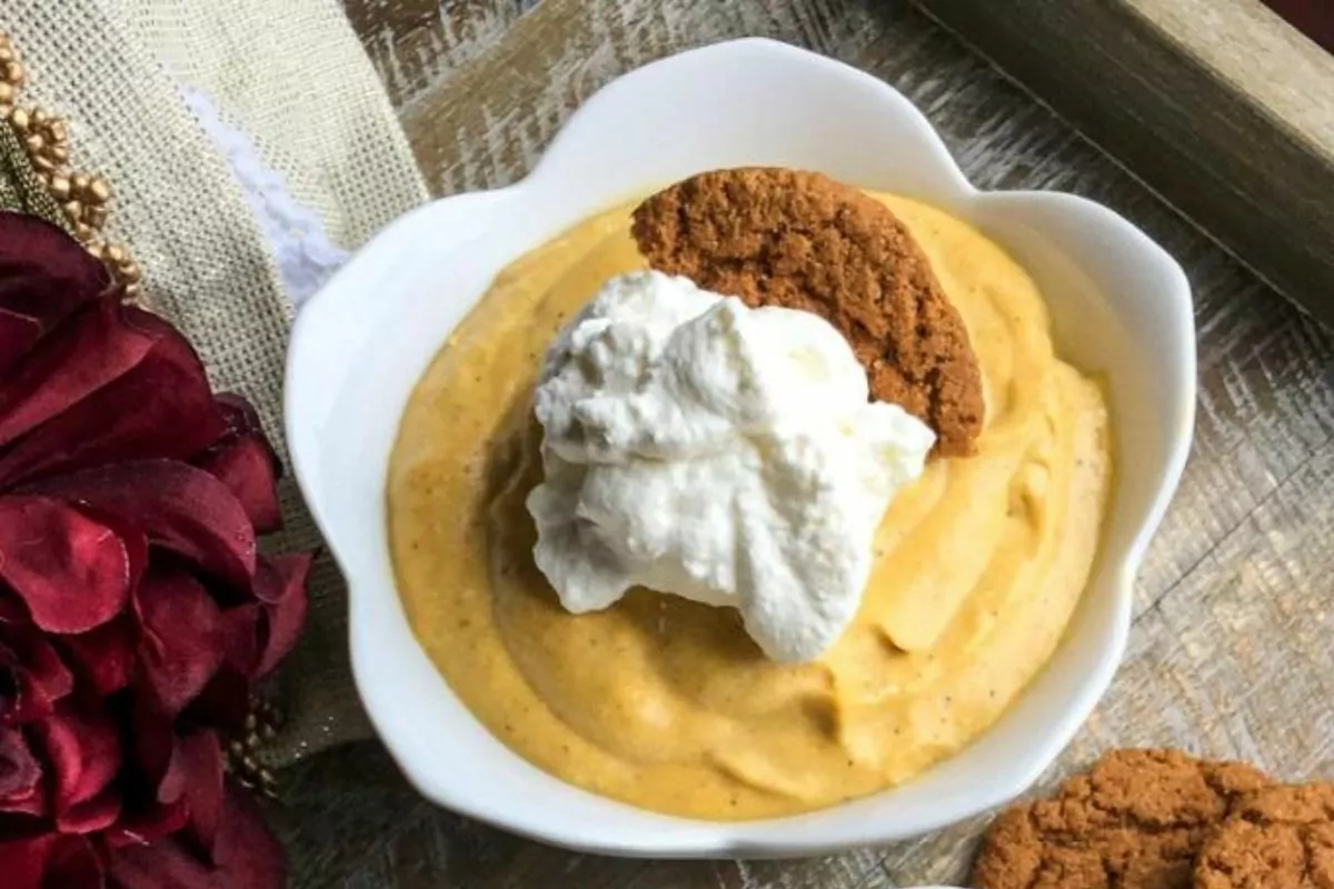 pumpkin mouse topped with whipped cream and gingersnap cookies served in a white flower shaped dish.