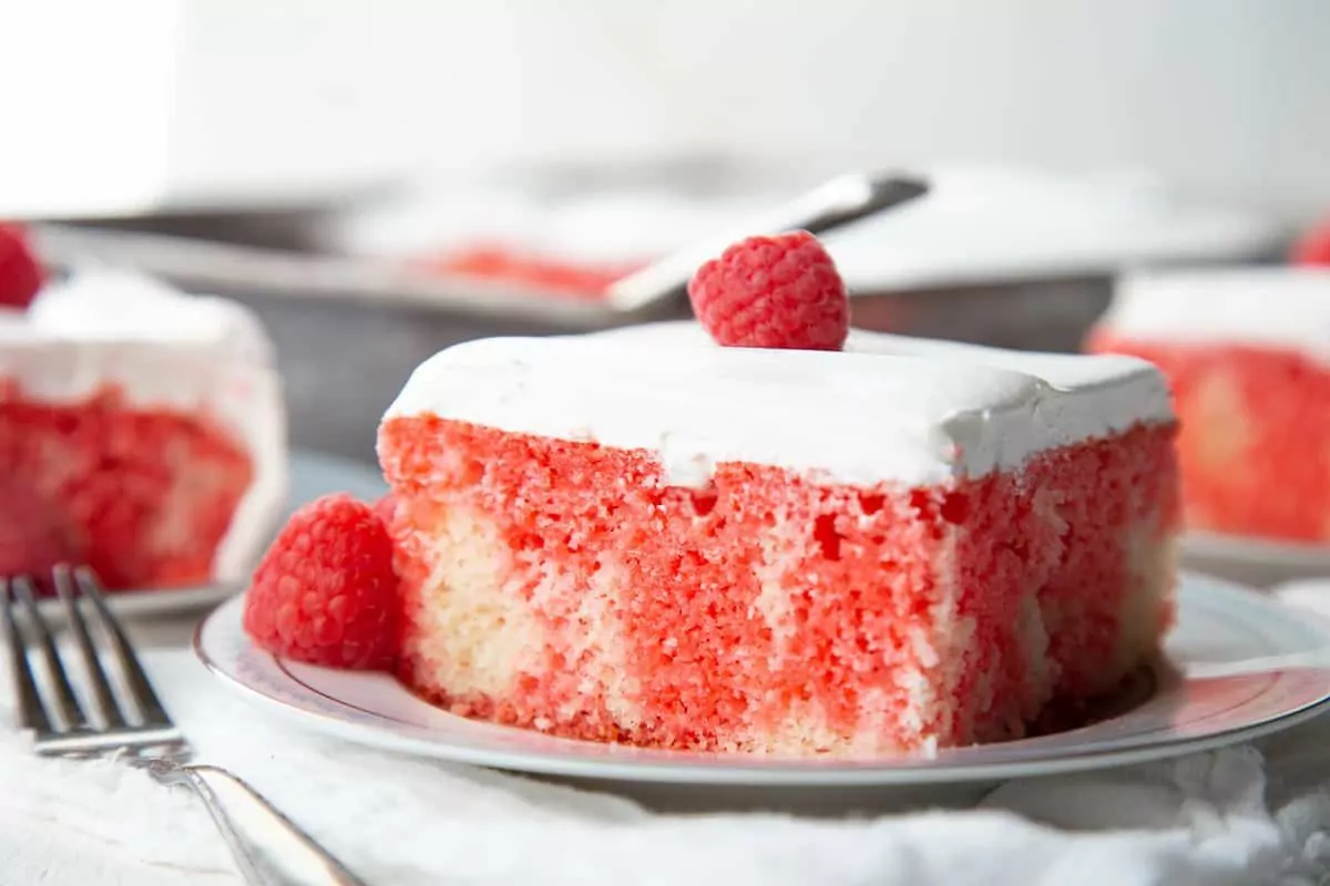 A slice of white and pink poke cake with fluffy white frosting.