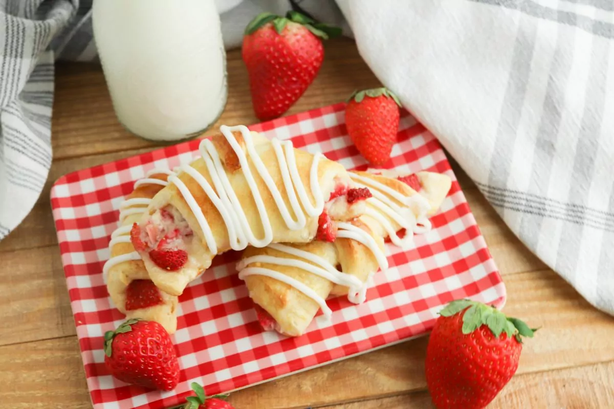 baked crescent rolls filled with cream cheese and strawberries on red checkered plate.