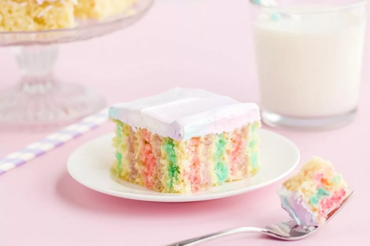 a slice of cake on a plate with three colors of jello and fluffy frosting.