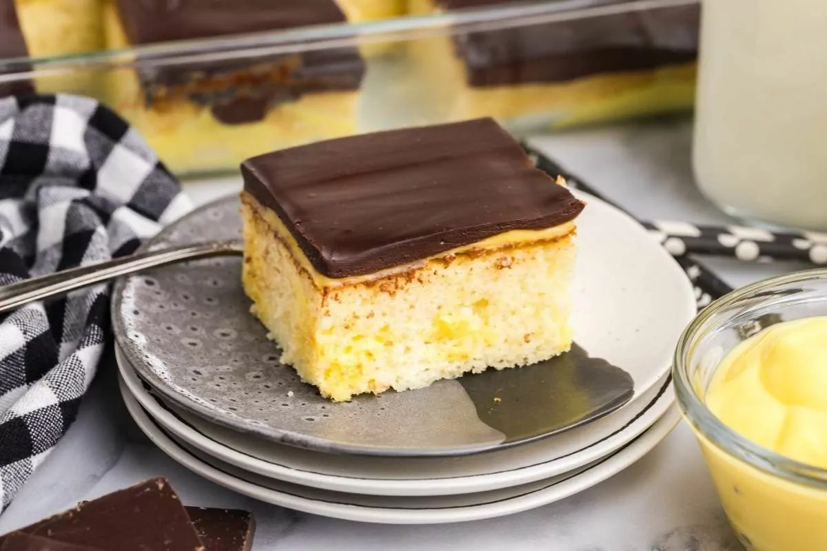 a slice of Boston cream poke cake on a plate with layers of cake, pudding and chocolate.