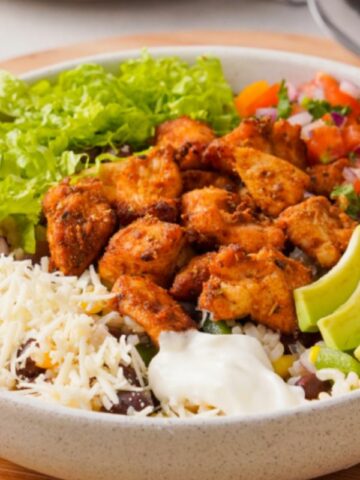 A bowl of chicken, rice, vegetables and sour cream.