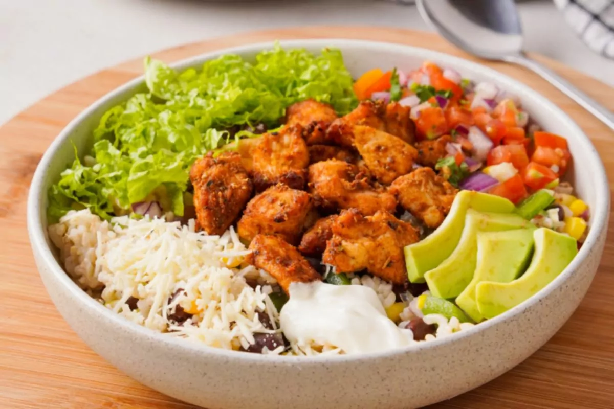 A bowl of chicken, rice, vegetables and sour cream.