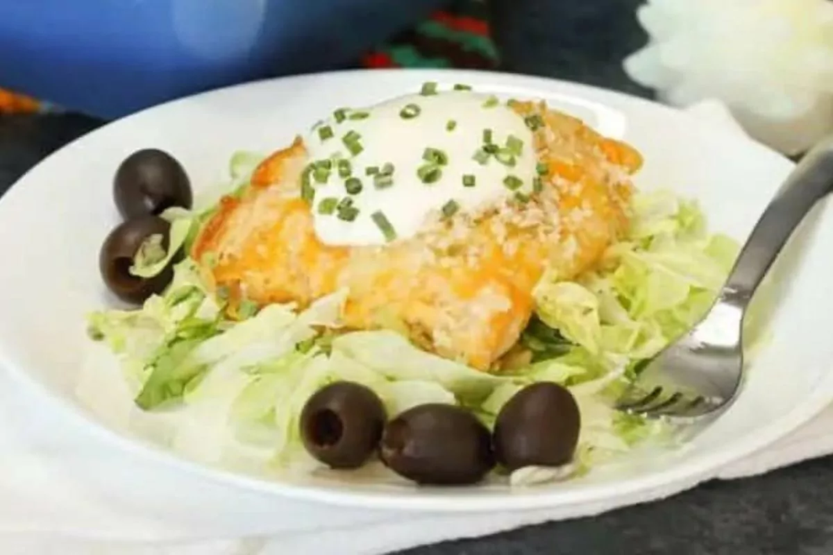 a plate of chicken enchiladas with black olives and lettuce.