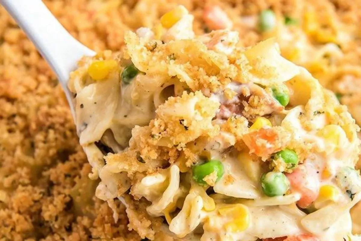 A serving spoon lifting creamy chicken noodle casserole from a serving dish.