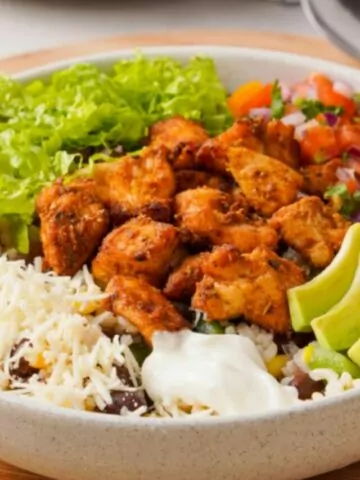 A bowl of chicken, rice, vegetables and sour cream.