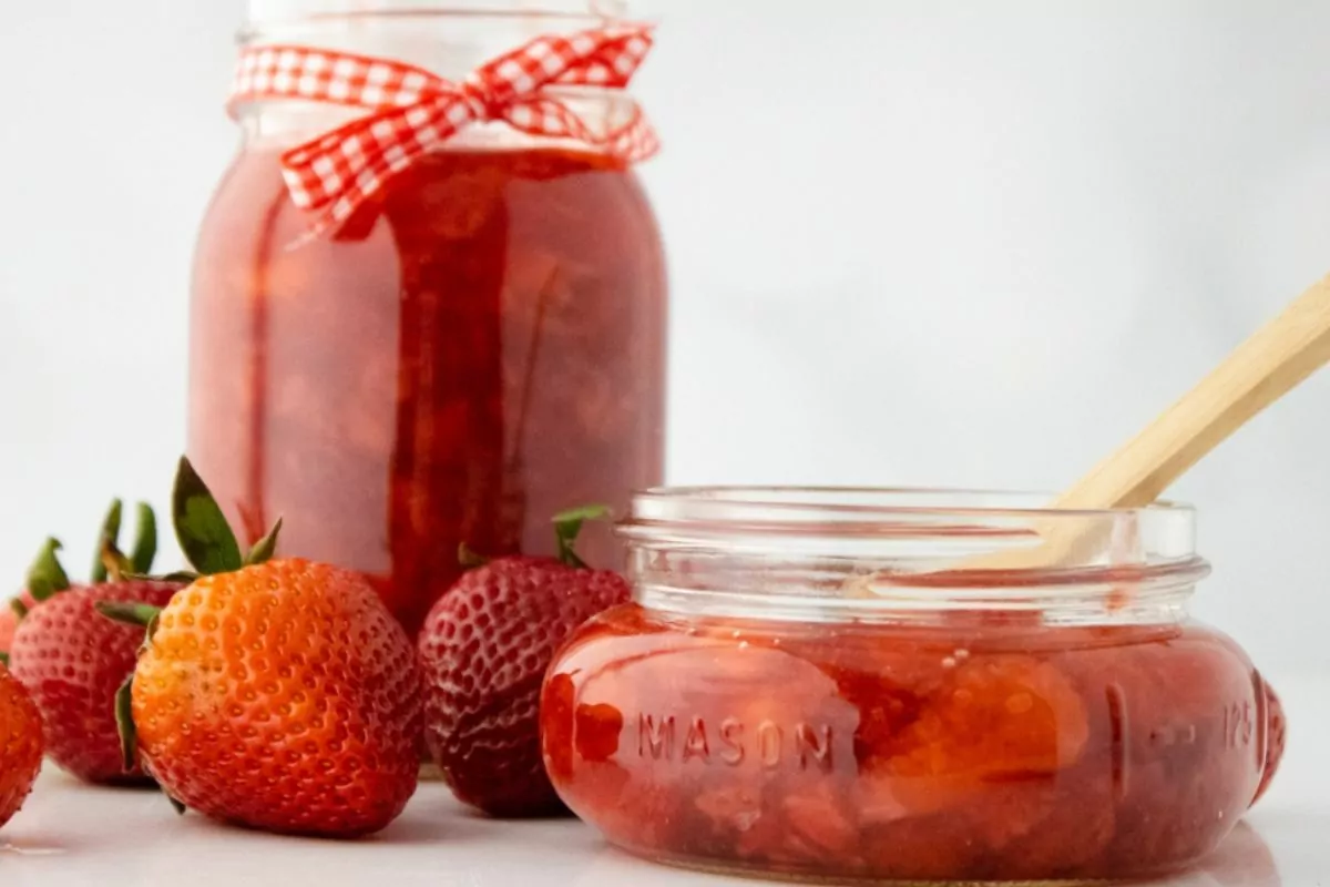 2 different jars of homemade strawberry sauce with fresh strawberries.