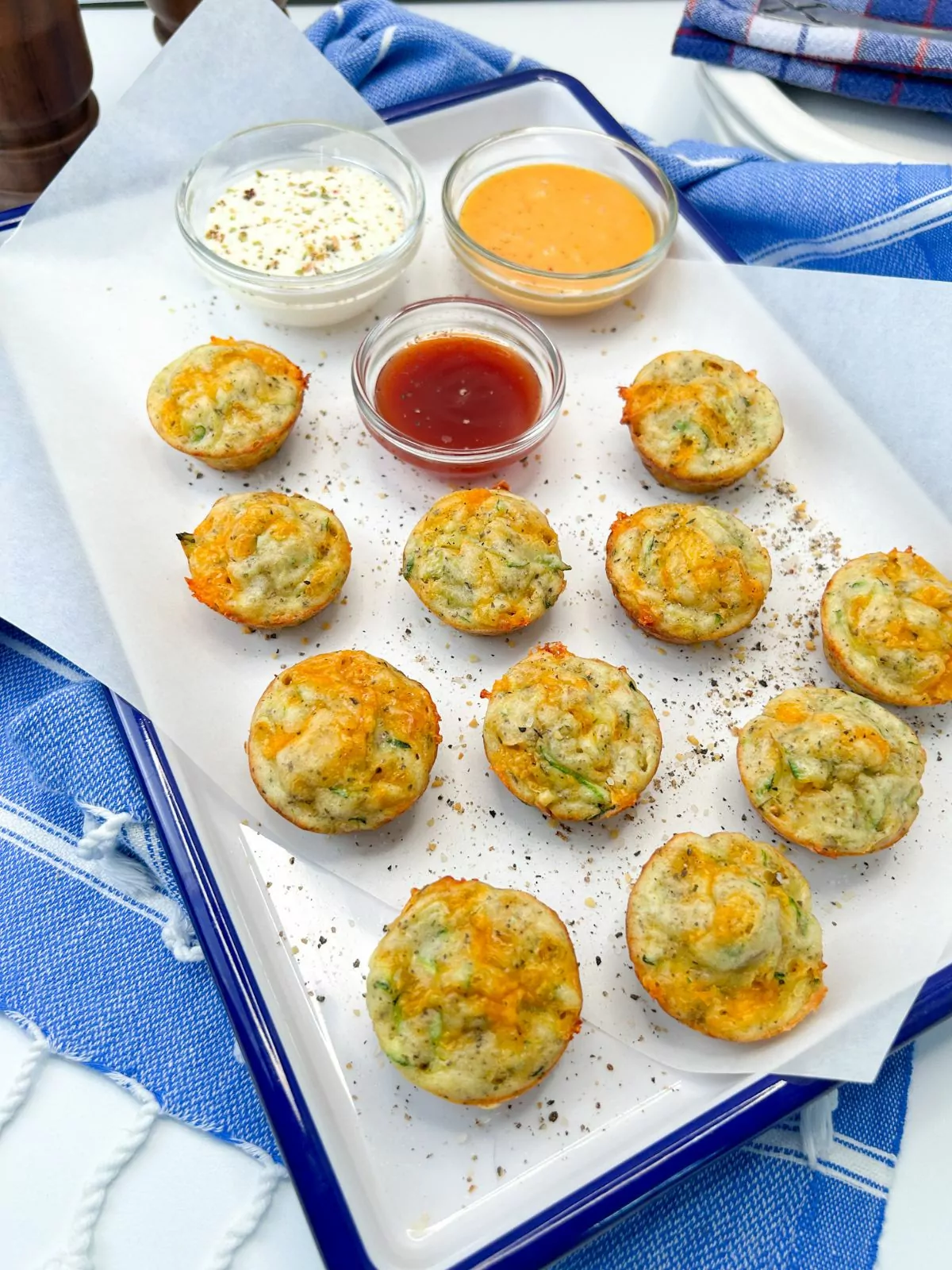 zucchini puffs on white tray with parchment paper and small bowls of dipping sauces.