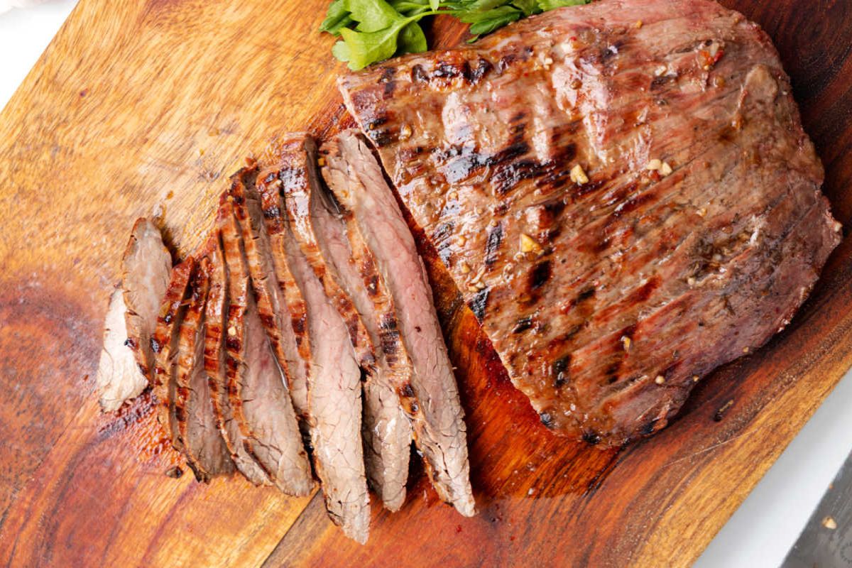 A flank steak on a cutting board, being cut into strips