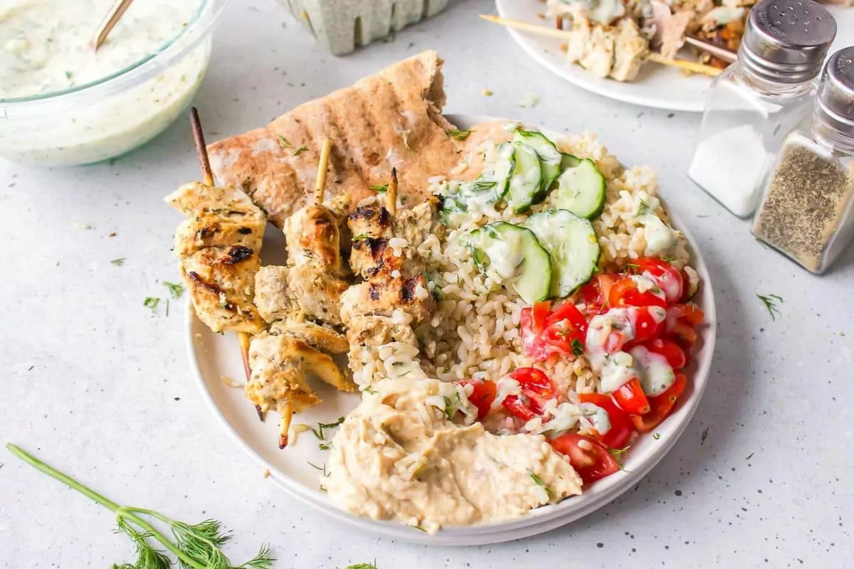 a plate with flatbread, greek chicken skewers, tomatoes and hummus