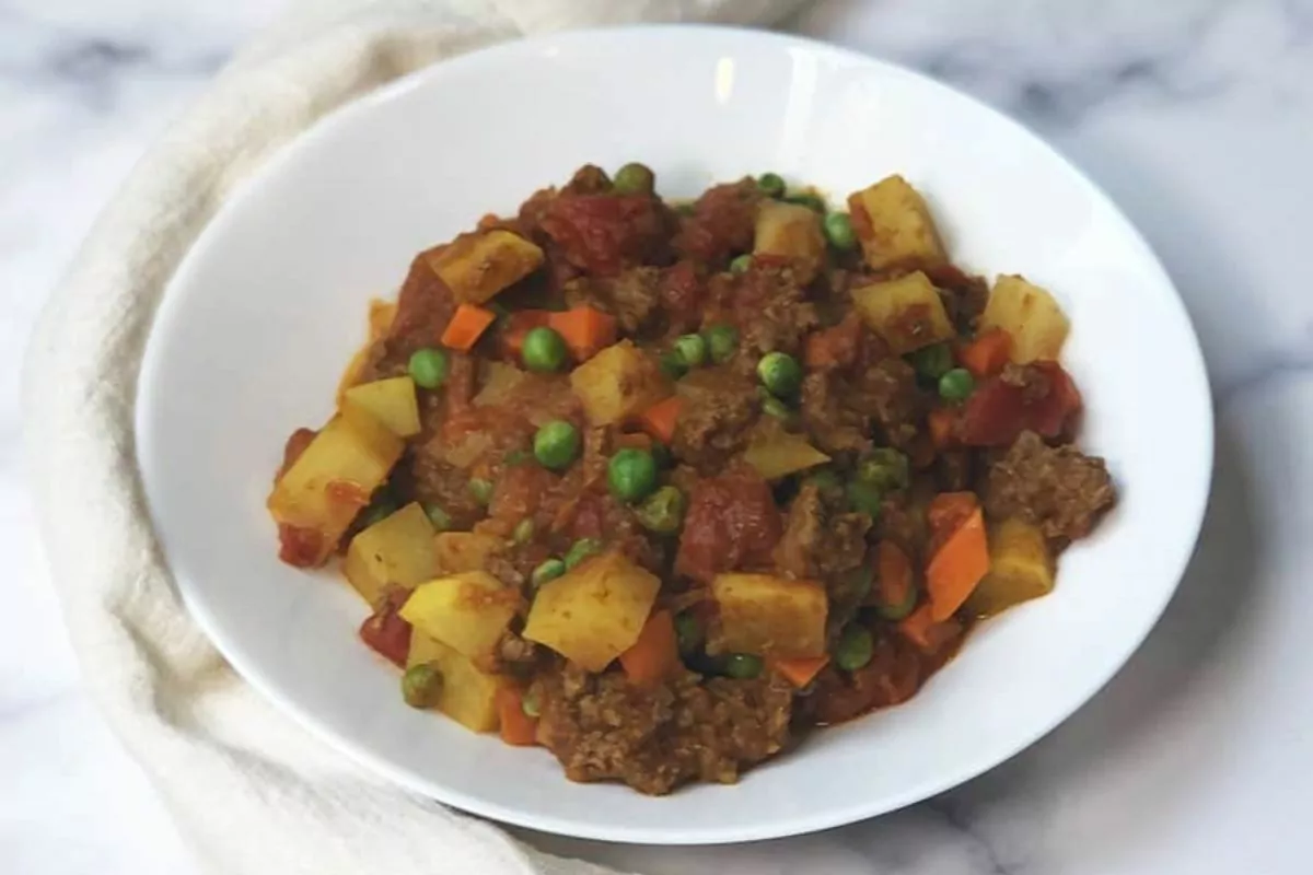 a plate of curry with potatoes, peas and ground beef.