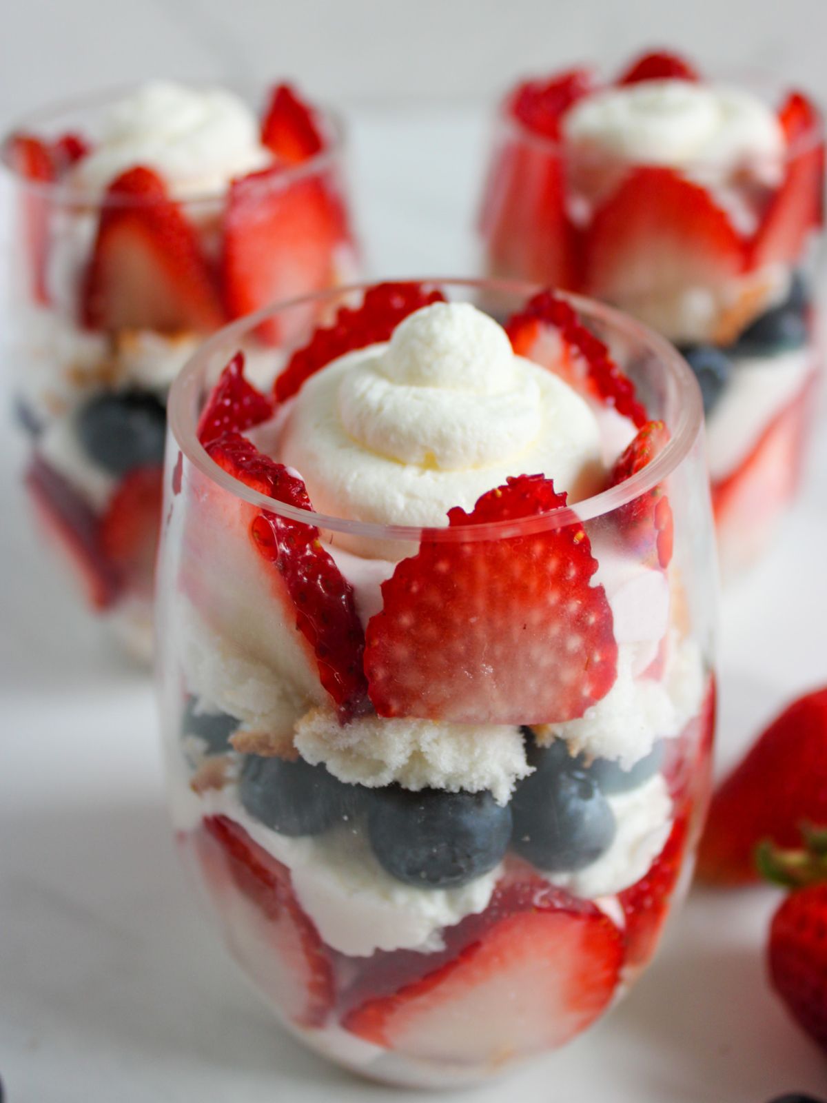 close up of three glasses of whipped cream and berries parfaits.