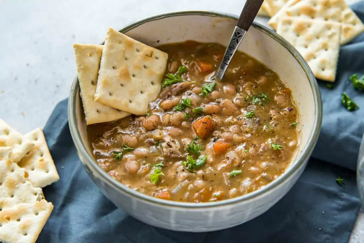 a bowl of bean soup with a spoon and crackers.