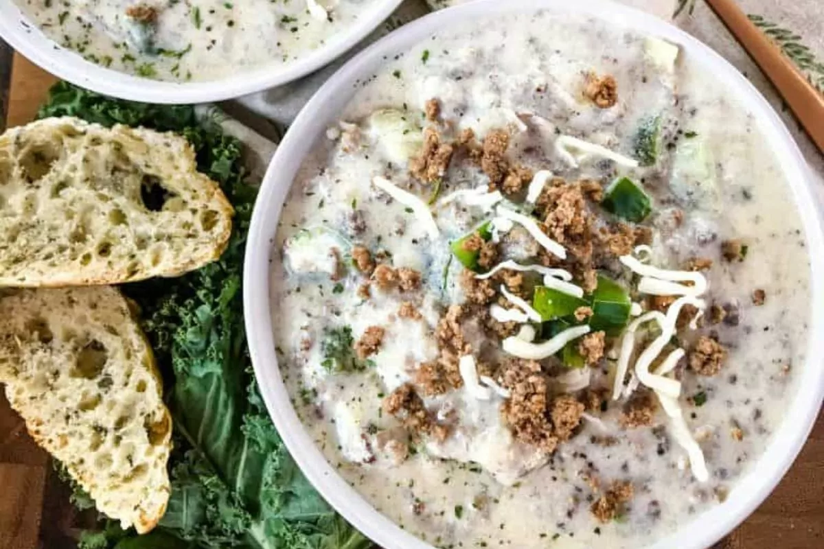 a bowl of creamy soup with ground beef, cheese, peppers and onions.