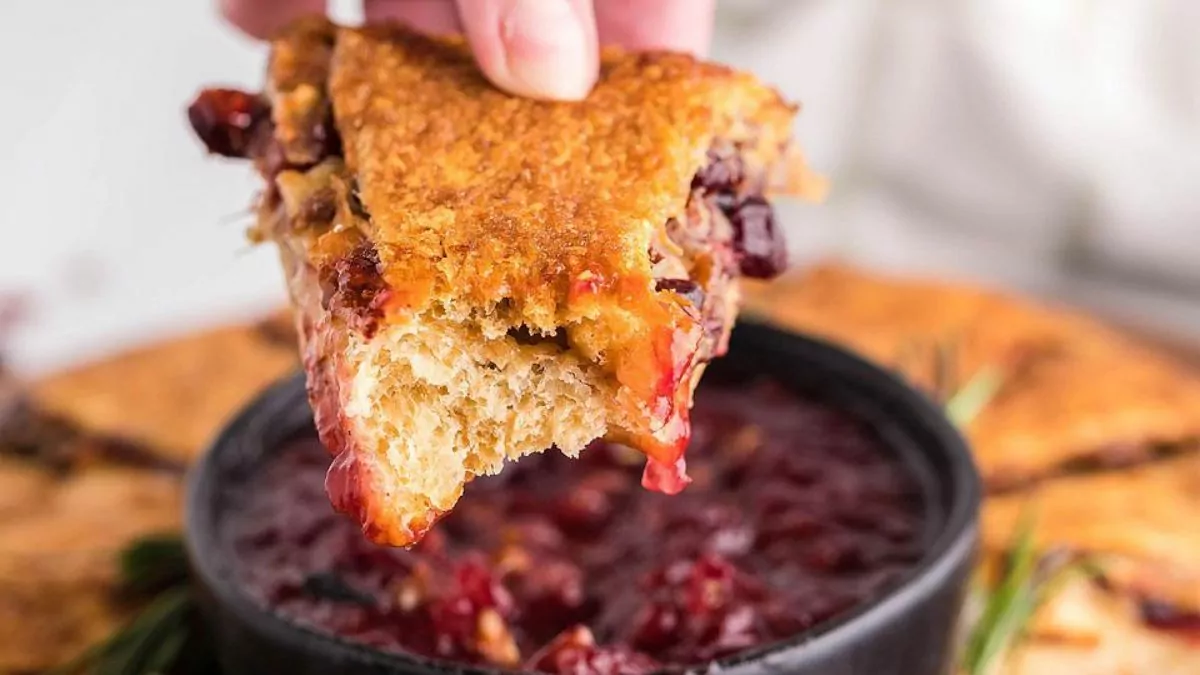 a serving of cranberry pineapple brie ring being dipped into cranberry sauce.