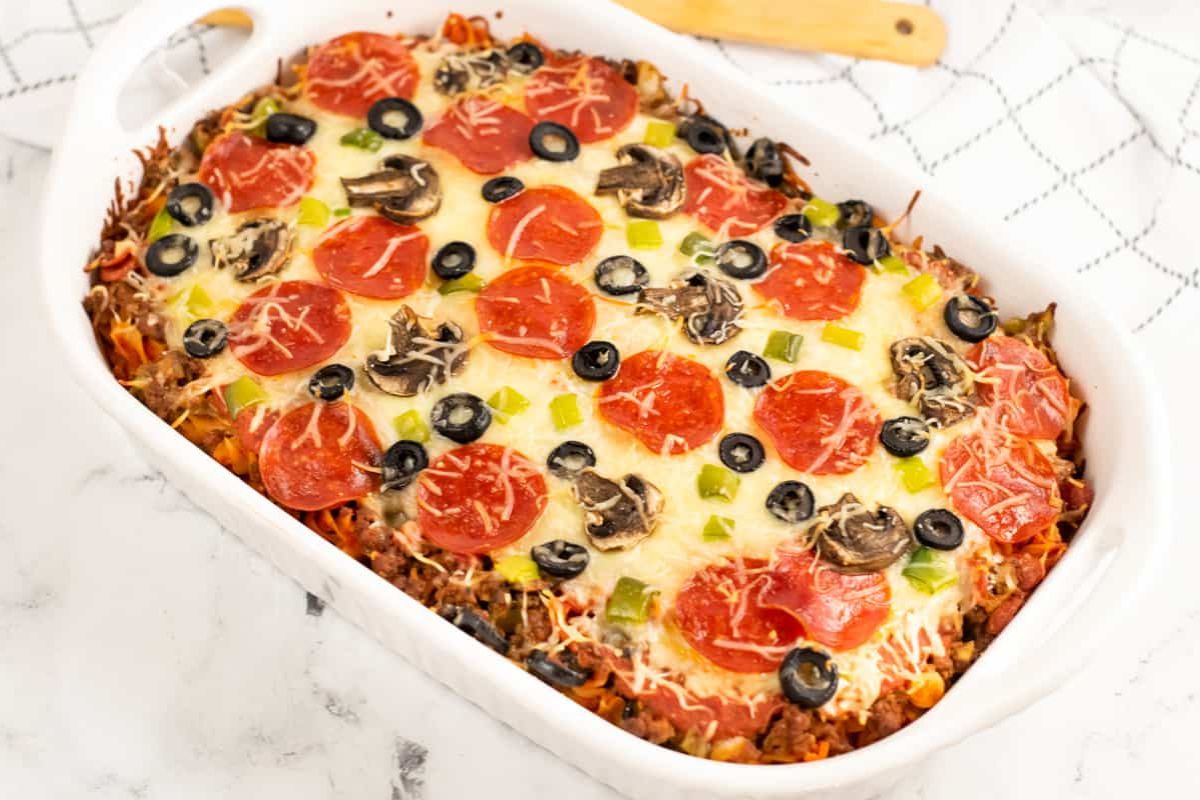 a casserole dish of pasta topped with pepperoni, cheese and olives.