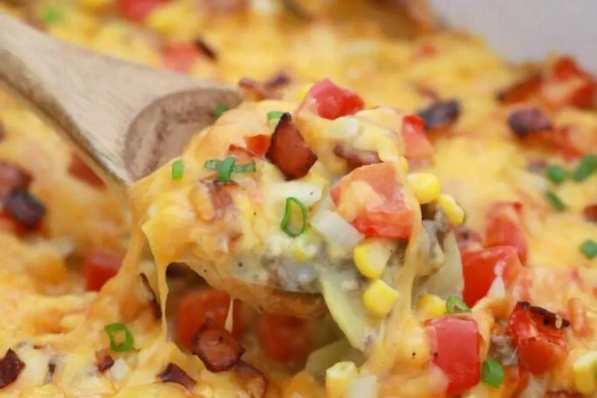 a casserole of potatoes, hamburger, cheese and bacon with a serving spoon.