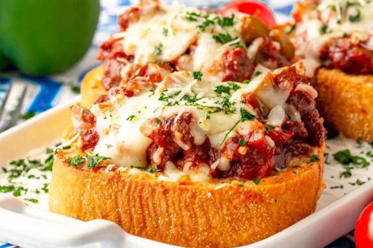 a sloppy joe piled onto a slice of thick garlic bread with cheese over top.