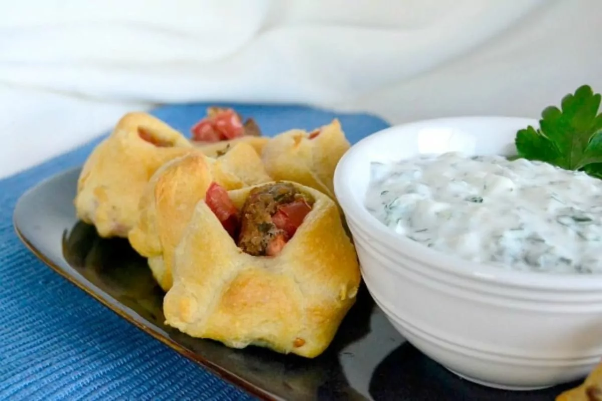 a plate with mini gyro bites with tzatziki sauce on the side.