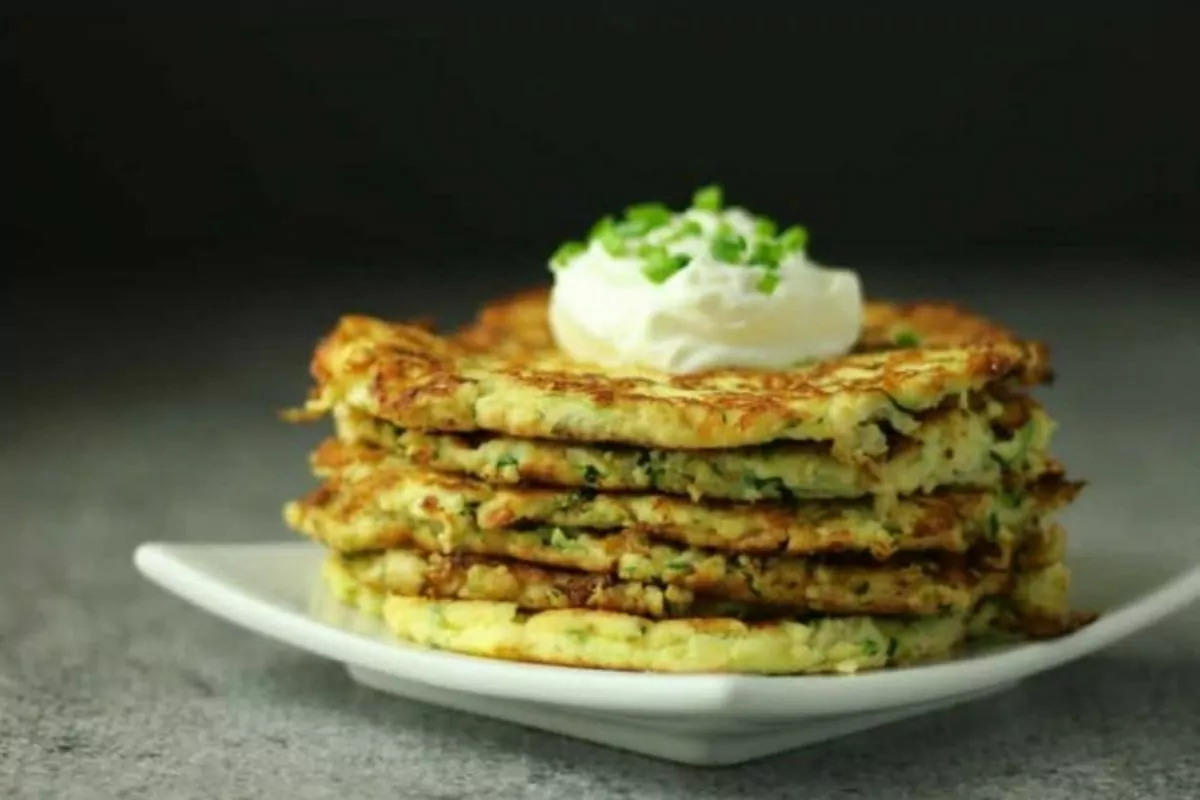 zucchini fritters with sour cream and chives on plate.