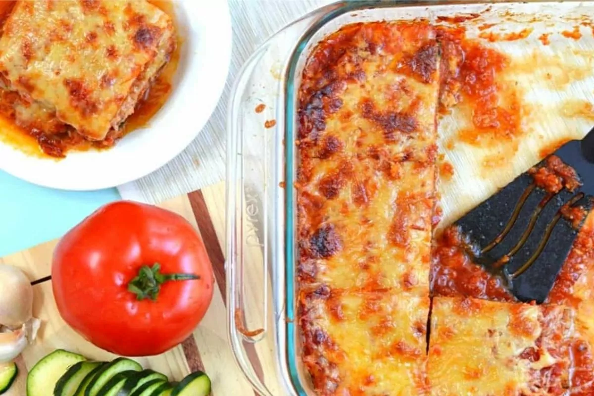 zucchini lasagna in casserole dish with whole tomato beside it.