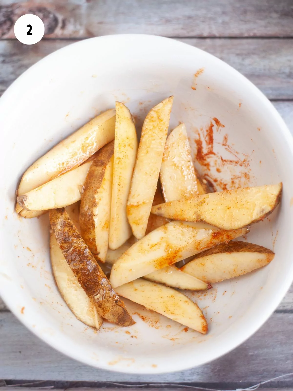 White bowl filled with potato wedges tossed in oil and seasonings