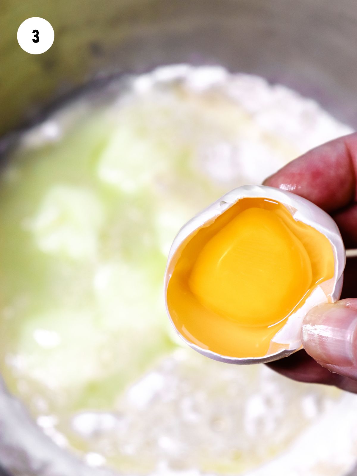 cracked egg about to be added to mixing bowl