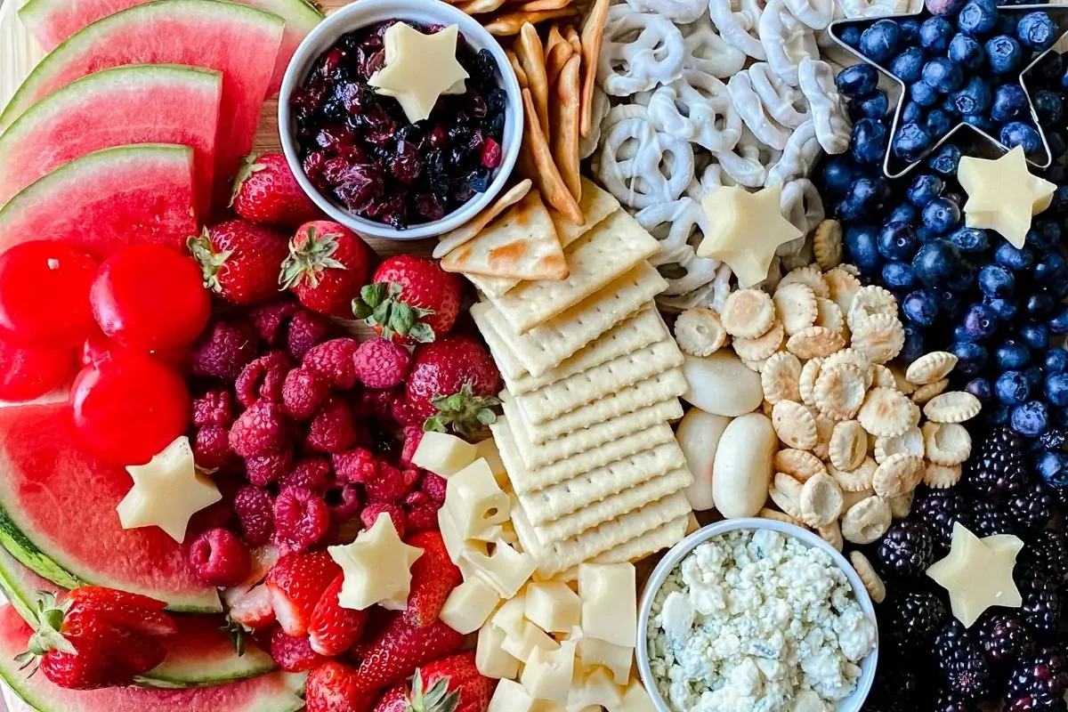 a board with assortment of cheeses, crackers, sweet and salty treats, and a bounty of fresh, seasonal fruit.