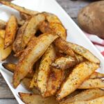 platter of air fried potato wedges with an air fryer and bottle of oil in the background