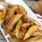 platter of air fried potato wedges with an air fryer and bottle of oil in the background