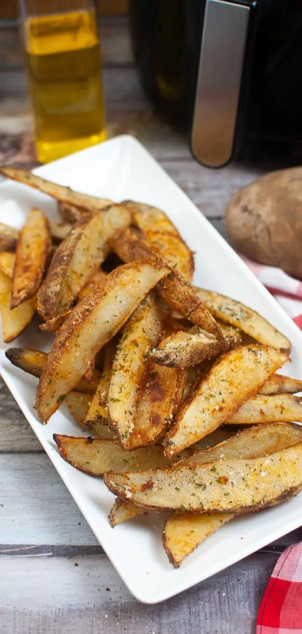 platter of air fried potato wedges with an air fryer and bottle of oil in the background