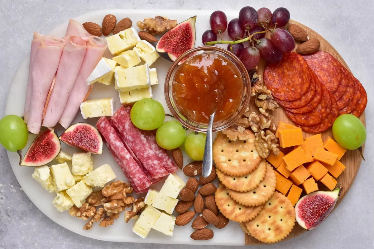 a board with cured meats, cheeses, nuts, seasonal fruit, crackers and a delicious jam spread