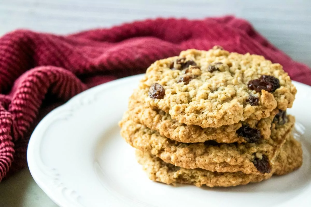 stacked oatmeal raisin cookies on a white plate with a red napkin.