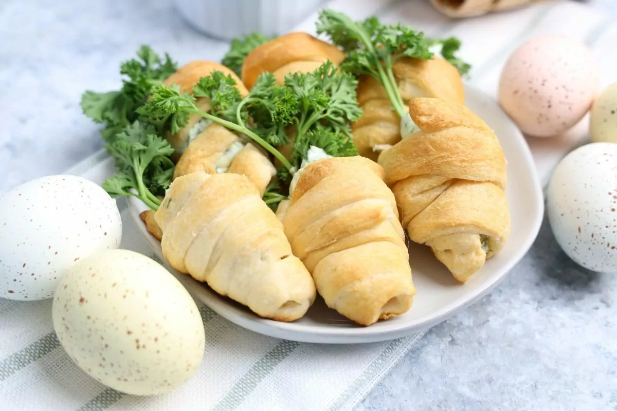 a plate of crescent rolls shaped like carrots stuffed with a dip surrounded by plastic eggs on top of a striped napkin.