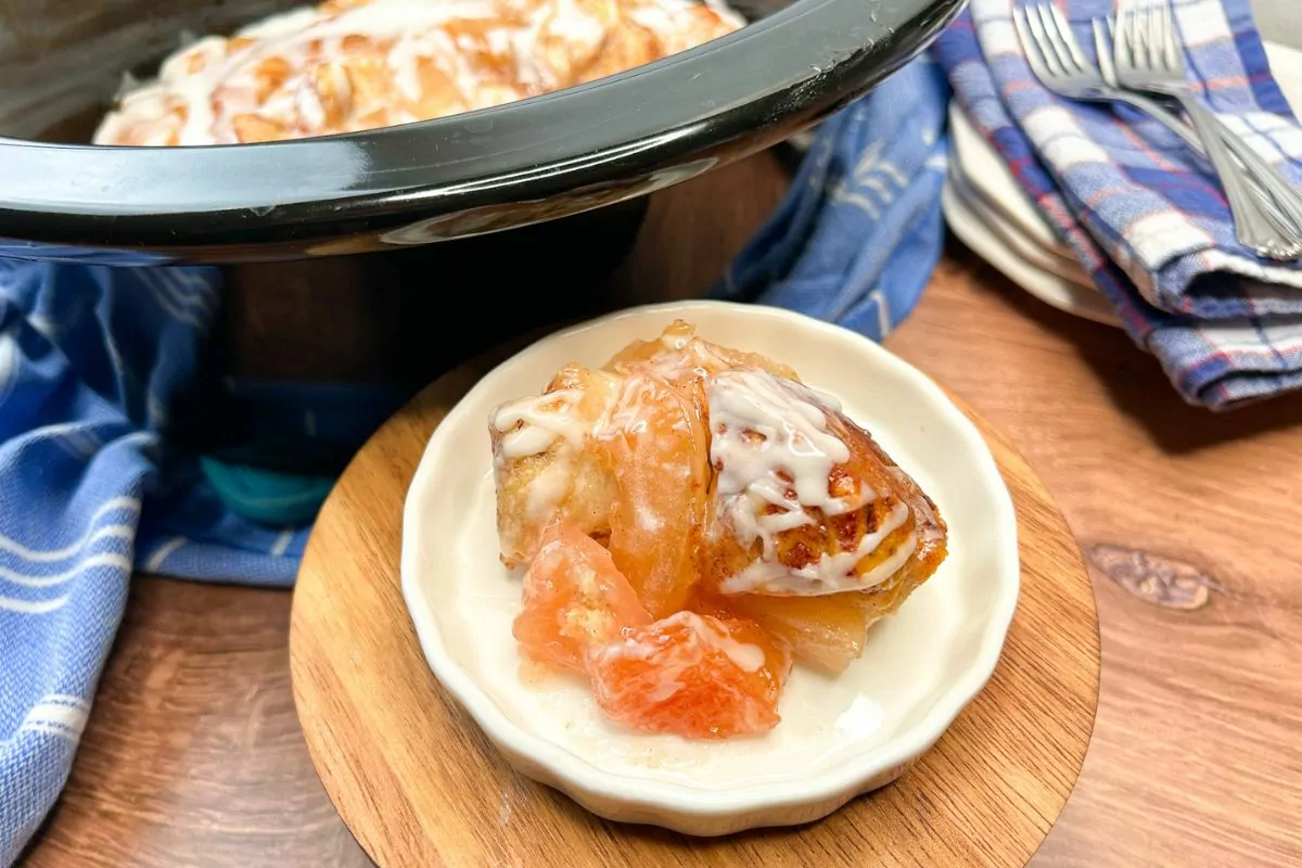 Crock Pot Cinnamon Rolls with Apple Pie Filling on a white plate and the crock in the background