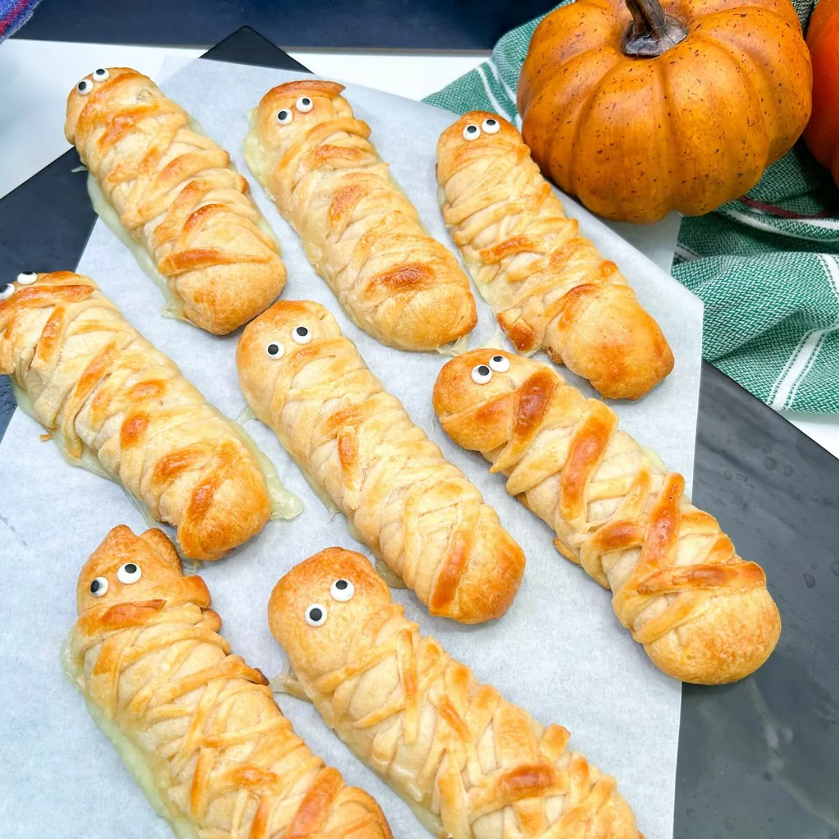 8 mozzarella sticks wrapped in crescent roll dough on parchment paper.