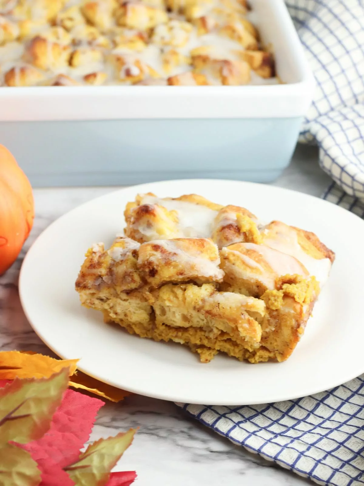 Pumpkin Cinnamon Roll Casserole served on a white plate with a light blue casserole dish in the background