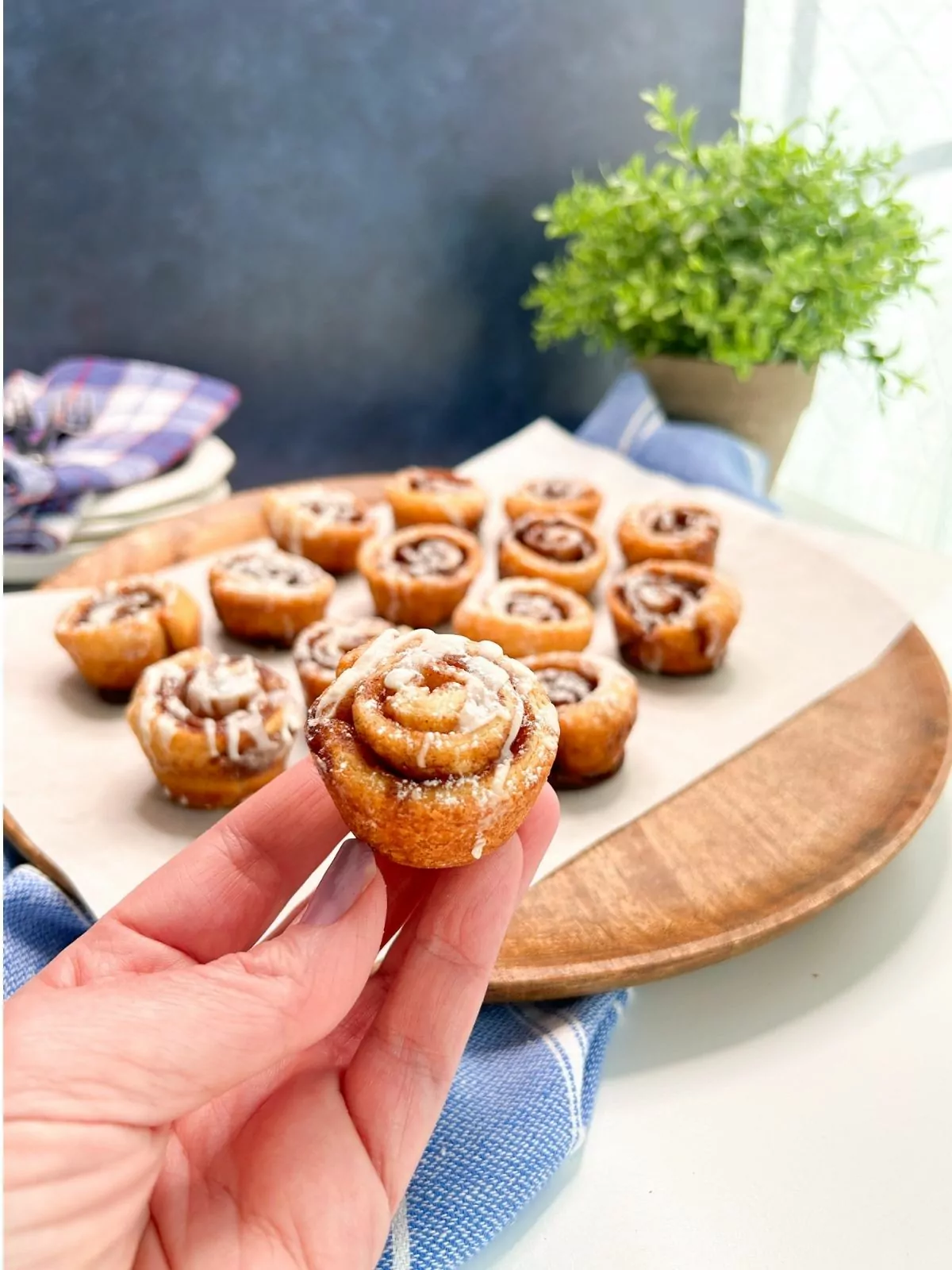 hand holding mini cinnamon roll over round board of other rolls.