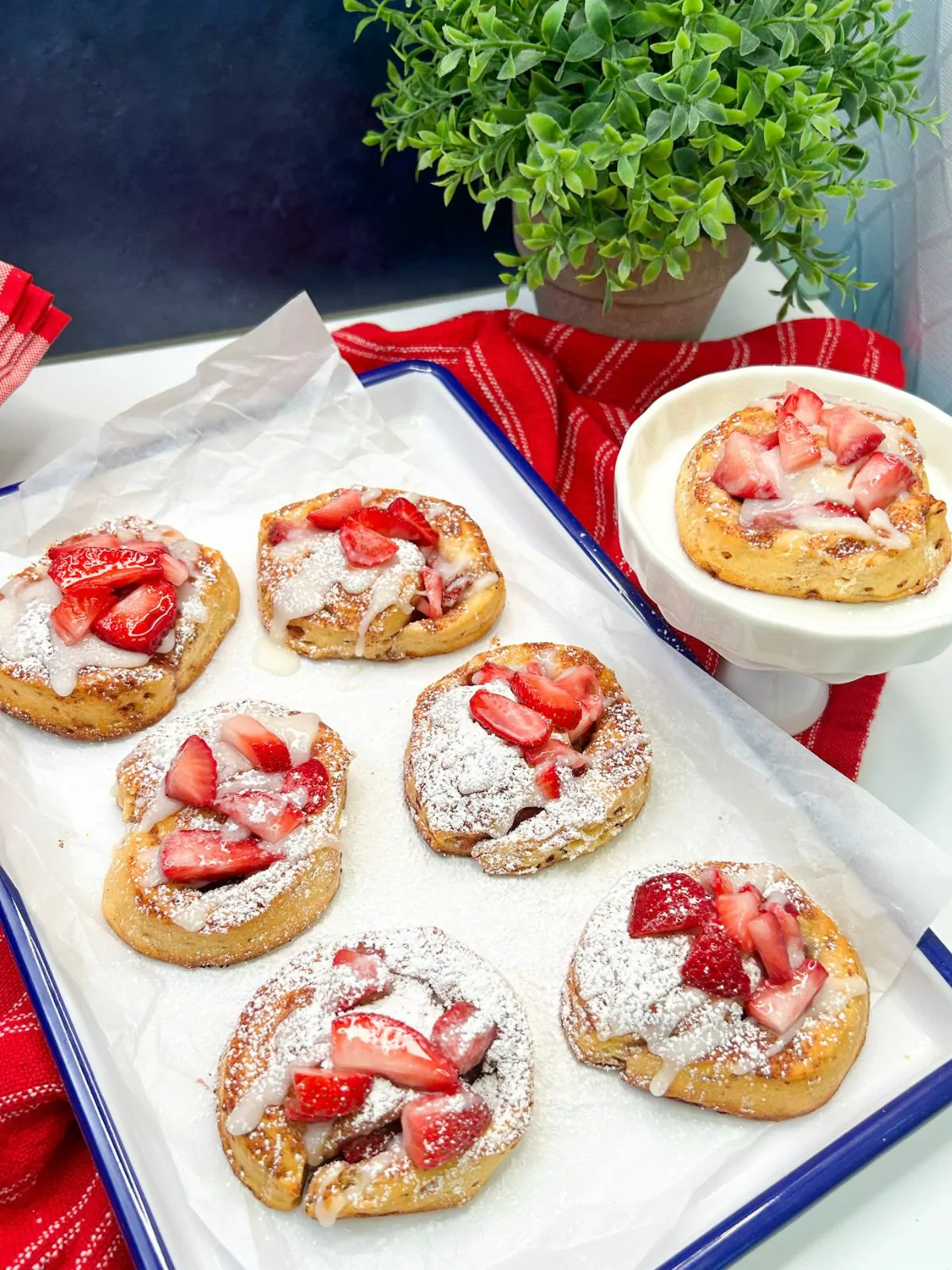 cinnamon rolls with powdered sugar and strawberries on white tray.