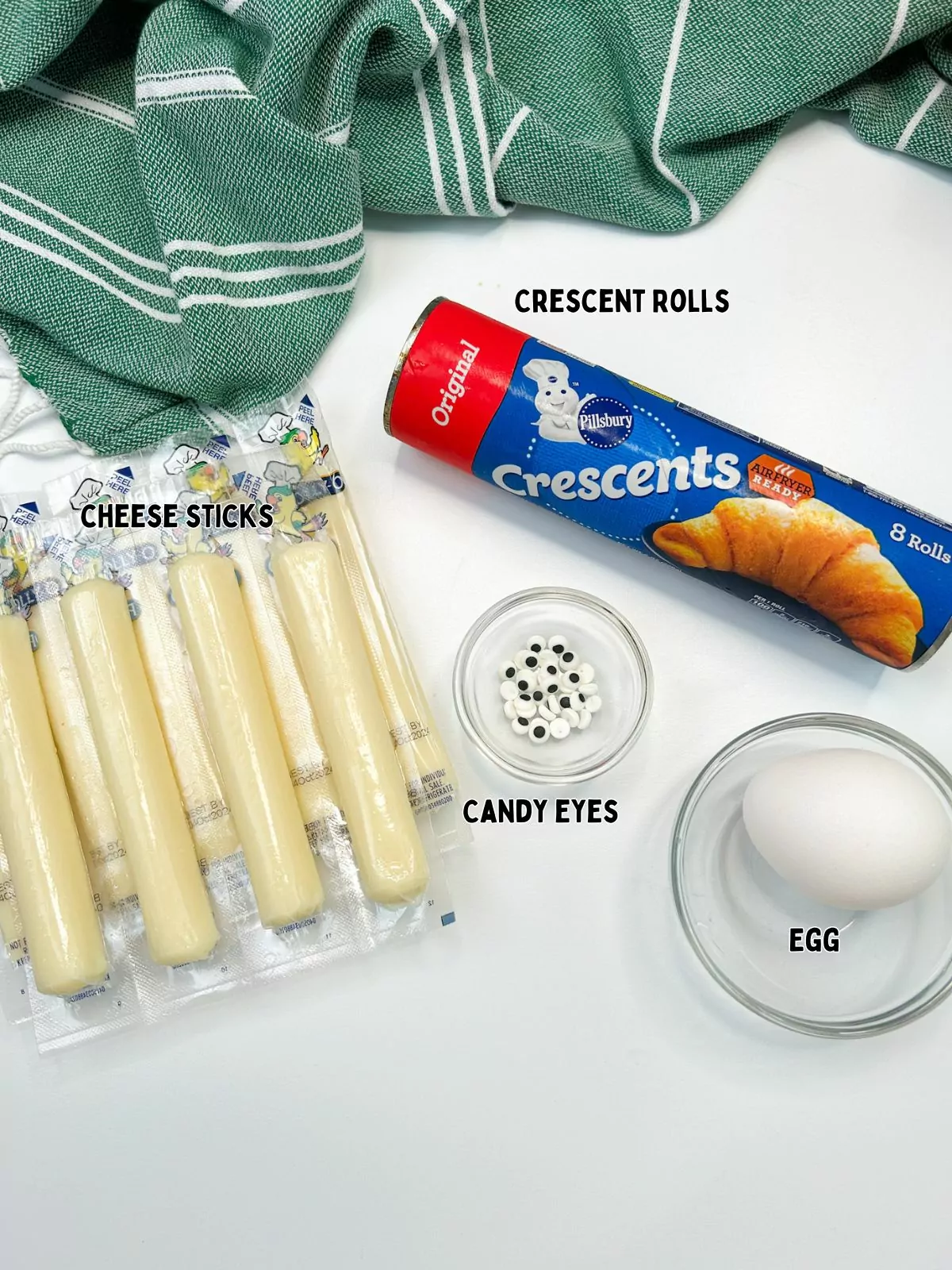 ingredients, crescent rolls, egg, candy eyes and wrapped mozzarella sticks.