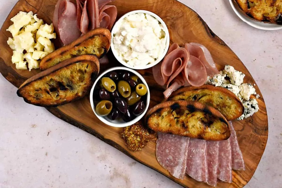 a charcuterie board with ham bread olive cheese and dip