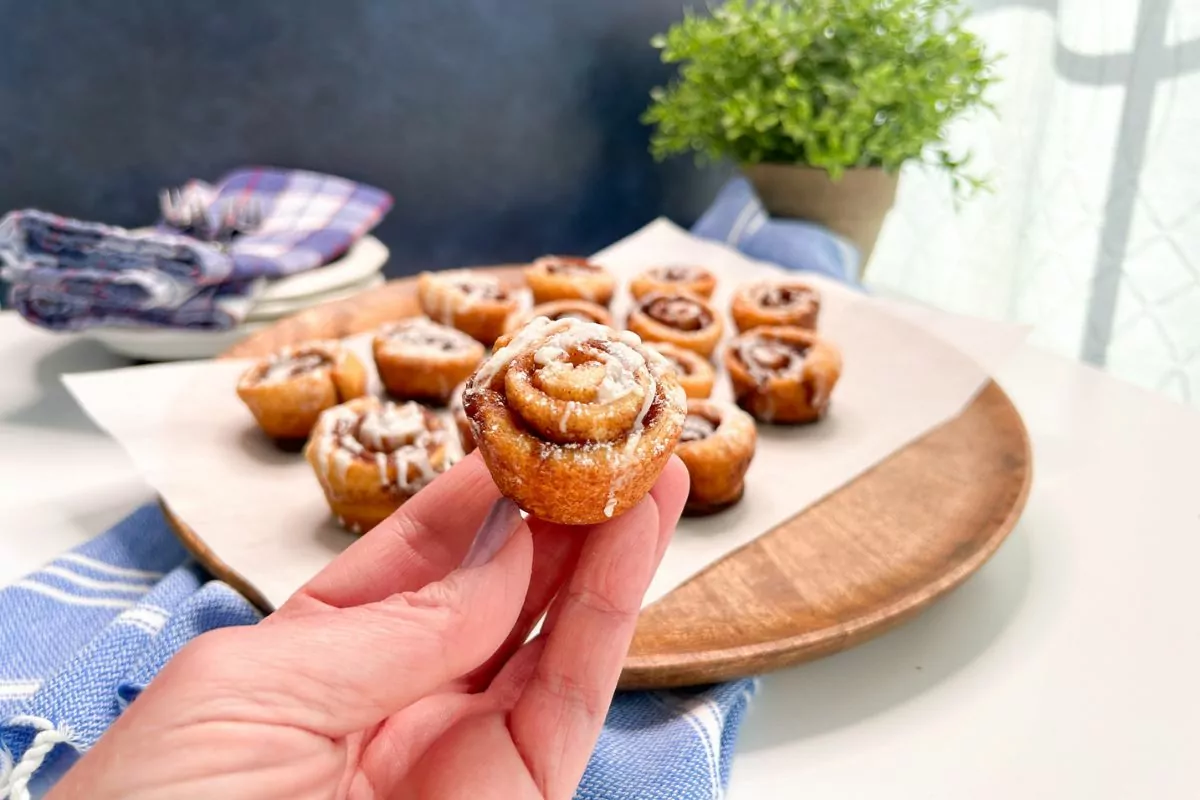 hand holding a mini cinnamon roll over a round board with more.