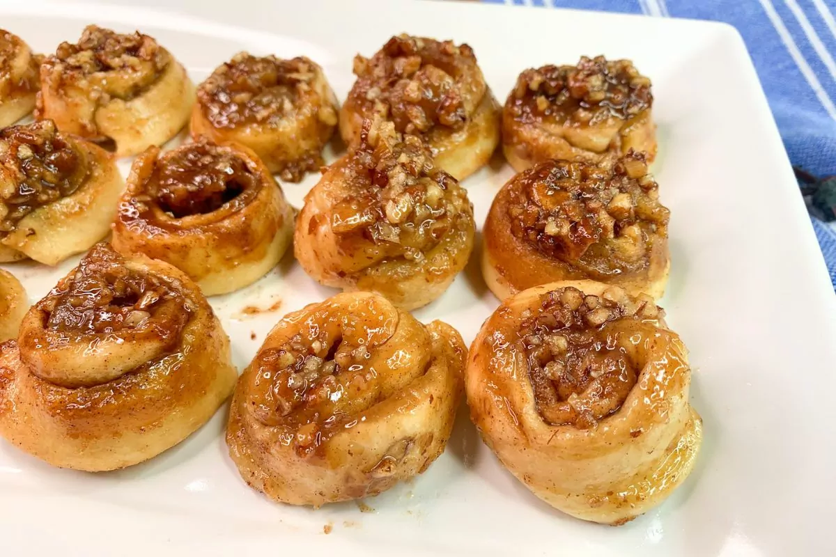 mini cinnamon rolls with pecan topping on white tray.