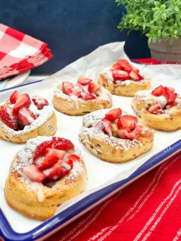 baked rolls with strawberries, glaze and powdered sugar on white tray.