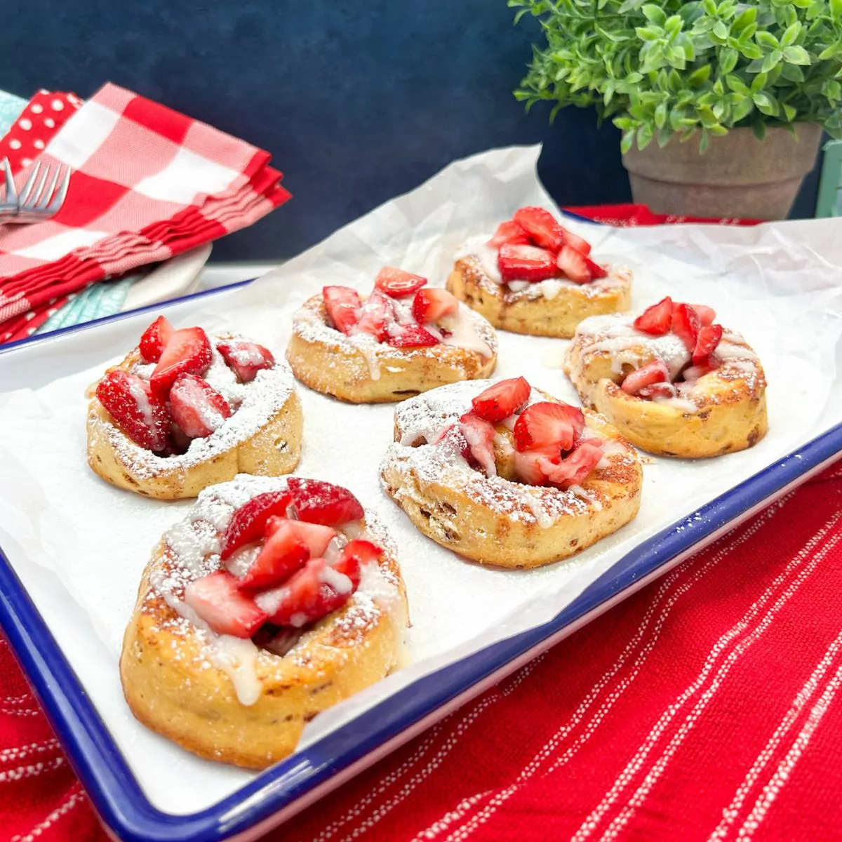 baked rolls with strawberries, glaze and powdered sugar on white tray.